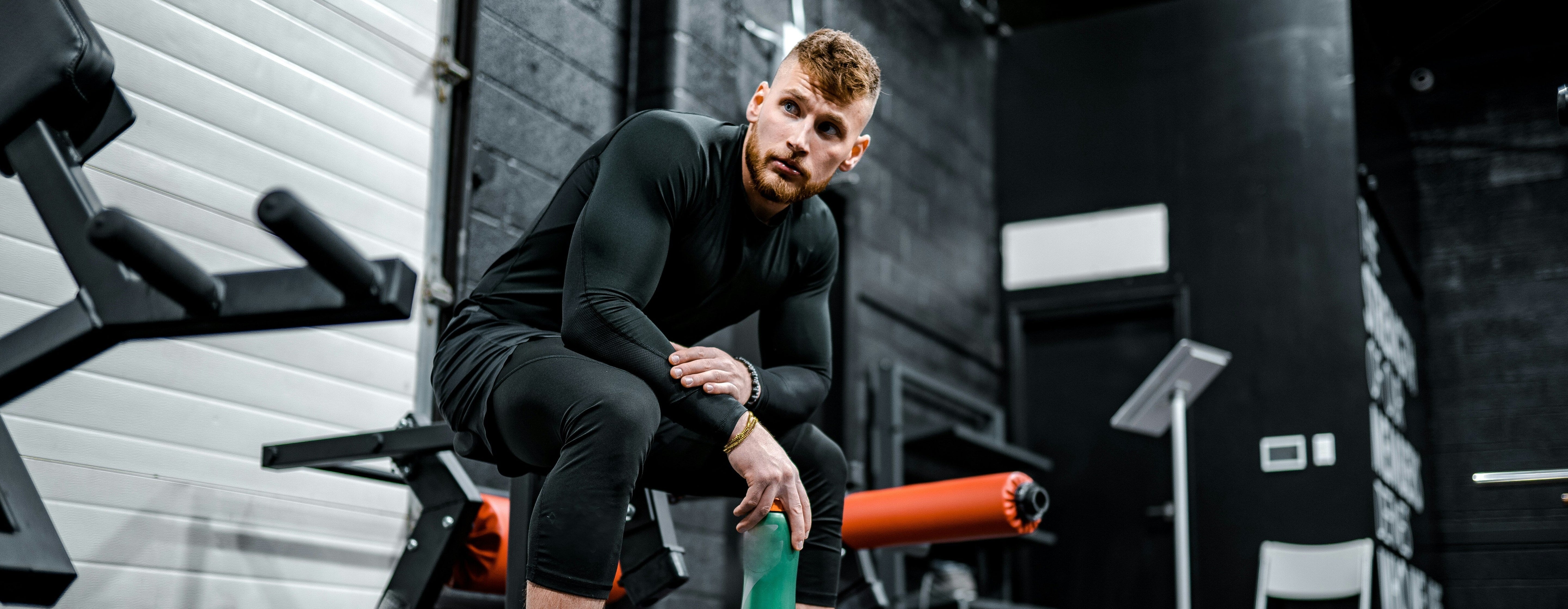 Athlet sitzt nach dem Workout im Gym mit Trinkflasche, Erholung und Deload Woche für bessere Regeneration