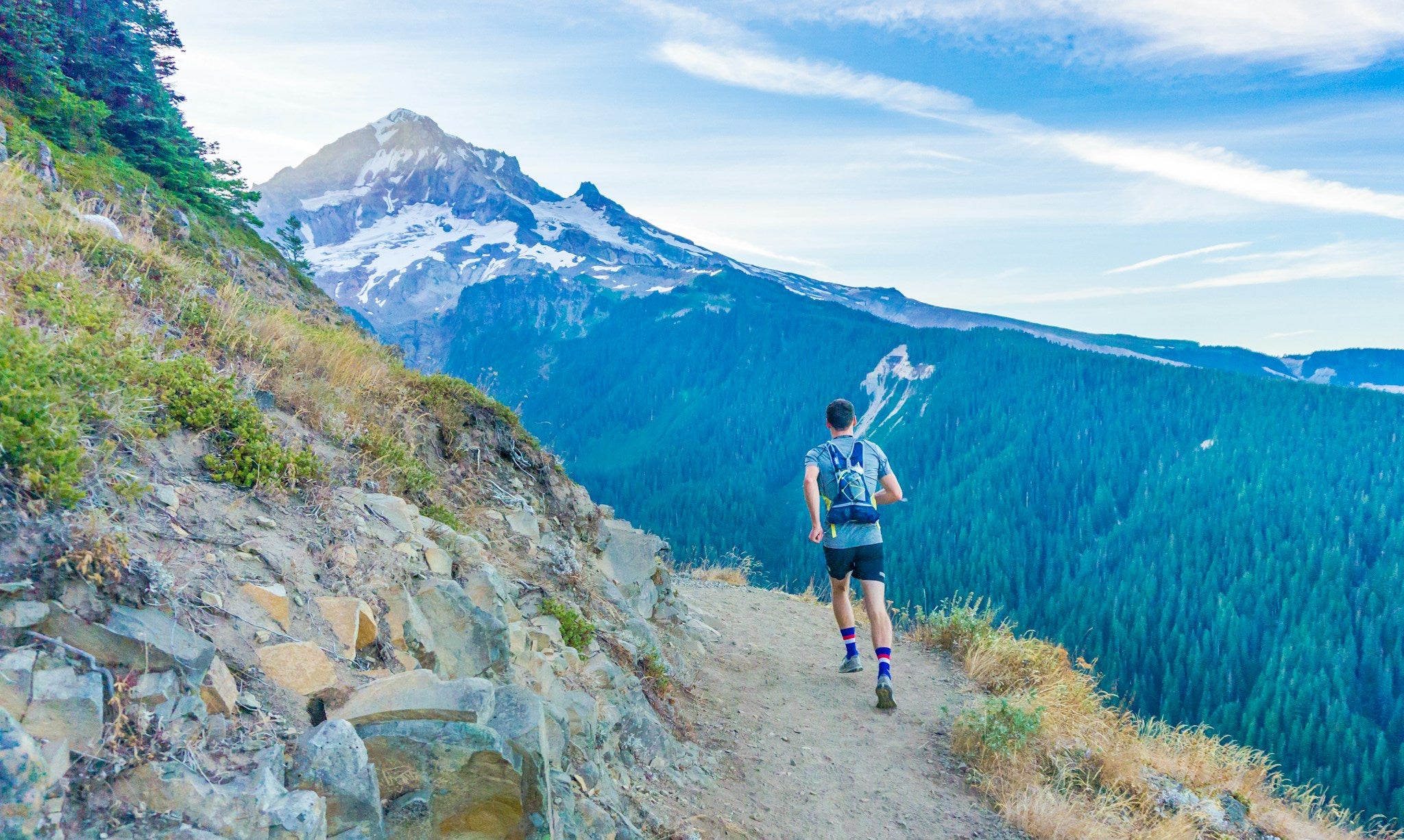 Trailrunner läuft auf einem schmalen Berggrat hoch über dem Tal – alpines Bergablaufen in den Bergen