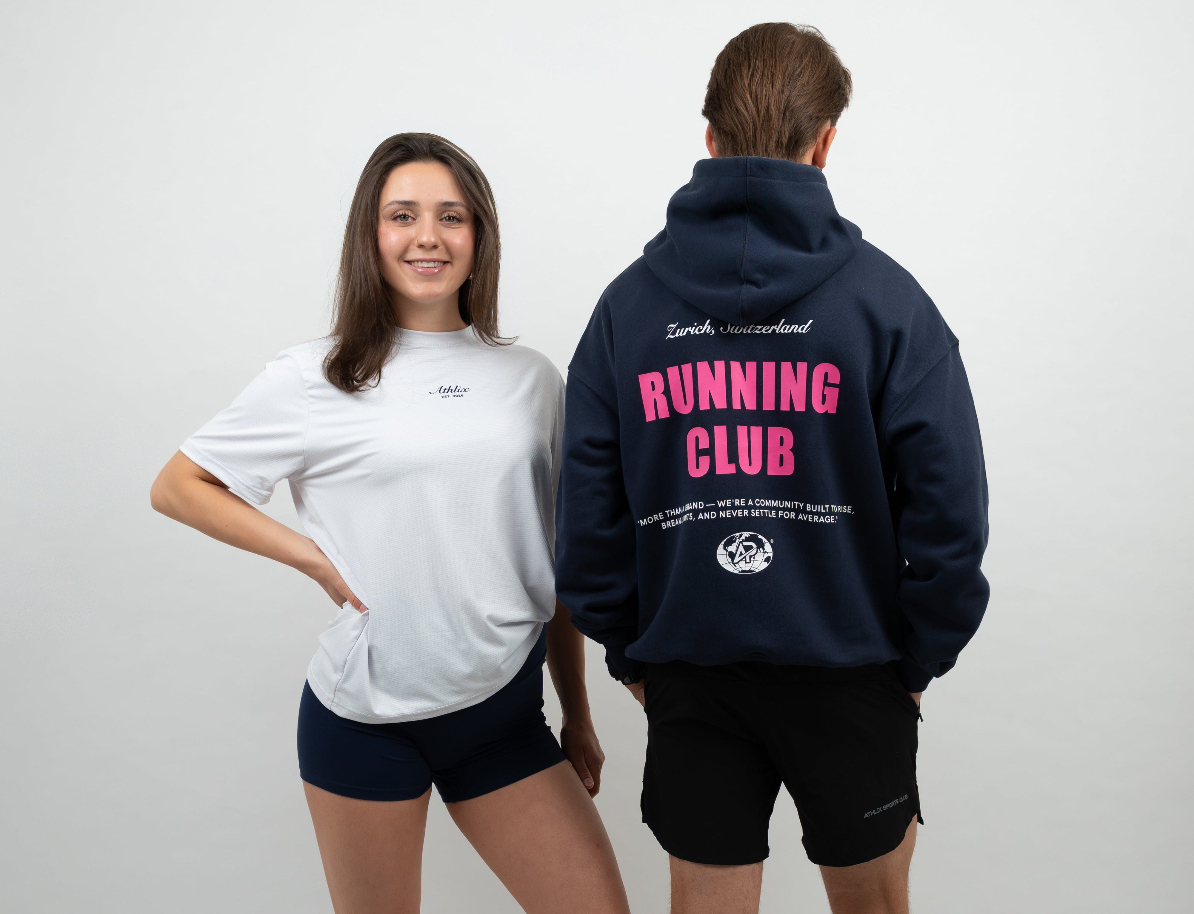 Zwei Models präsentieren den Athlix Running Club Hoodie in Navyblau mit pinker Schrift, aufgenommen im hellen Studio in Zürich.