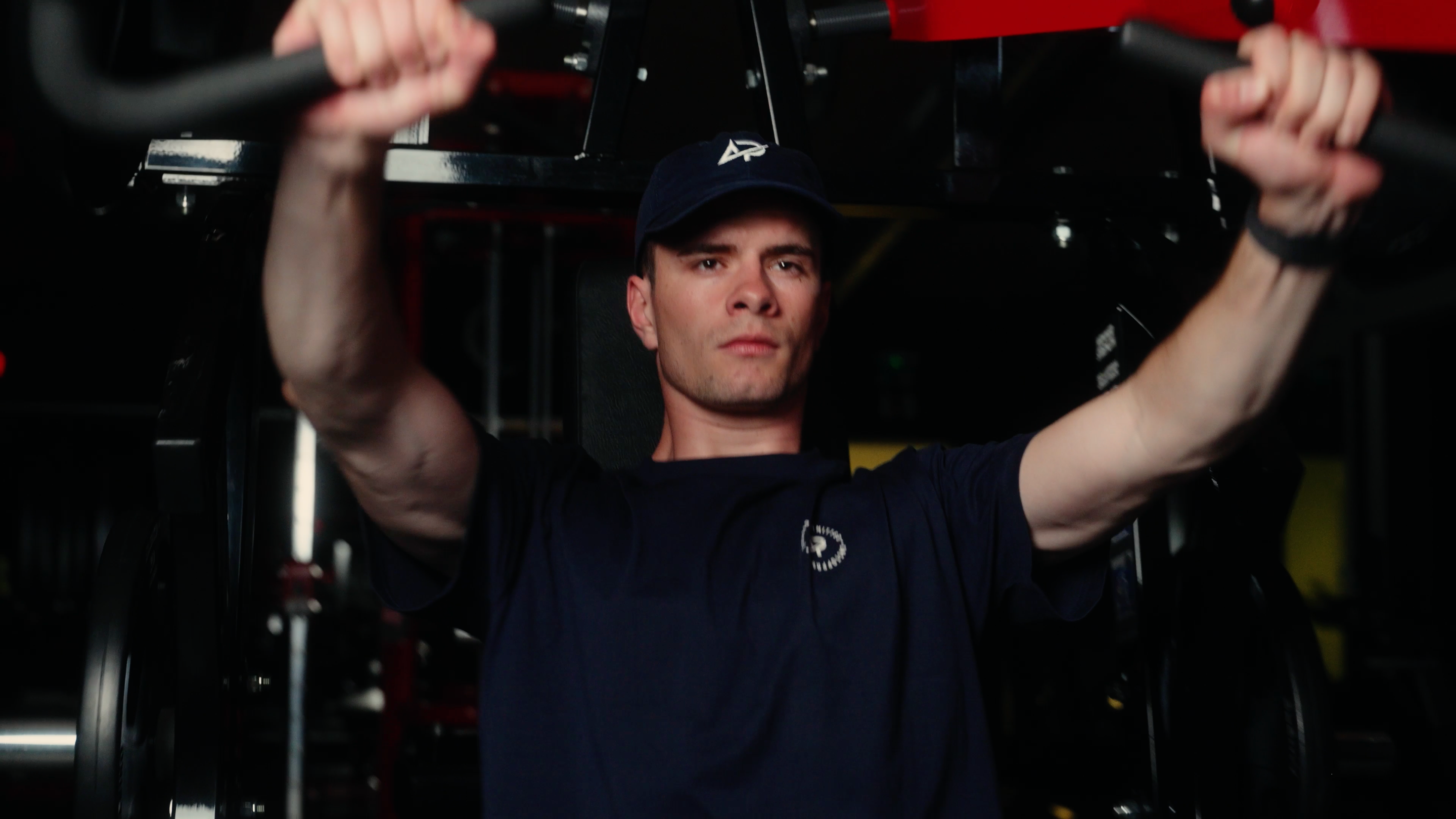 Junger Athlet mit dunklem Shirt und Cap trainiert konzentriert an der Klimmzugstange im Fitnessstudio.