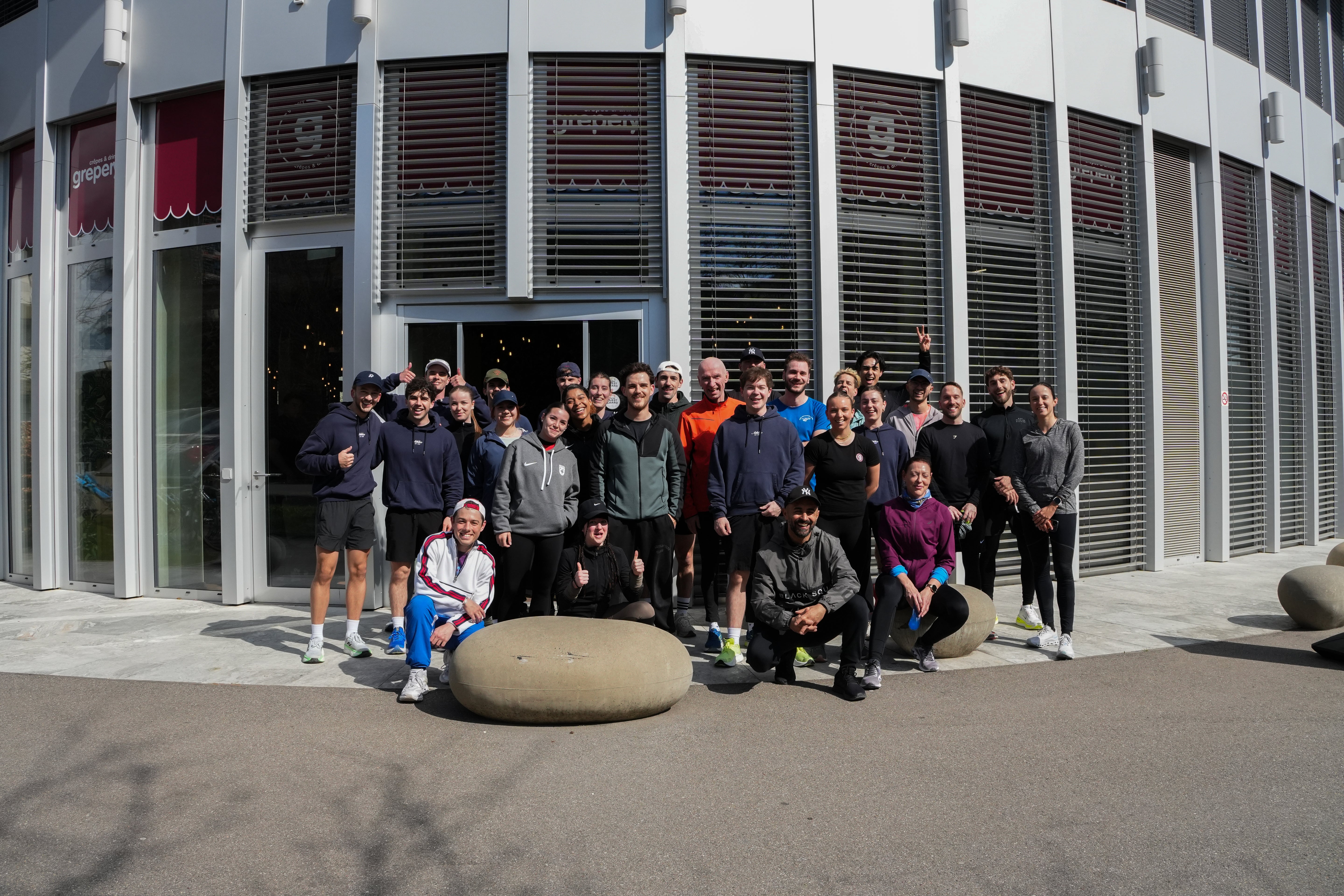 Grosse Trainingsgruppe von Athlix Performance versammelt sich vor einem modernen Gebäude für ein Gruppenfoto nach dem Outdoor-Training.