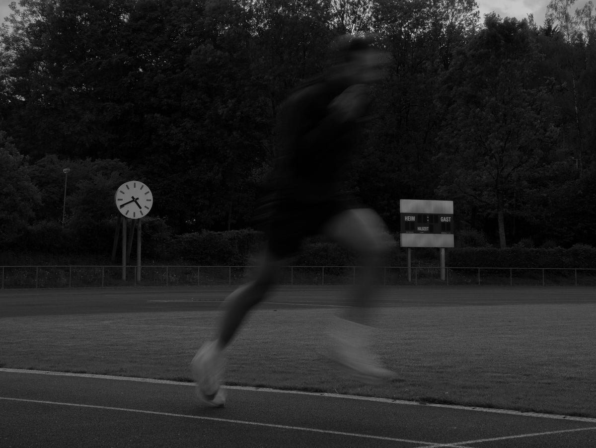 Läufer sprintet beim Schwellentraining über die Tartanbahn, Stadionuhr im Hintergrund