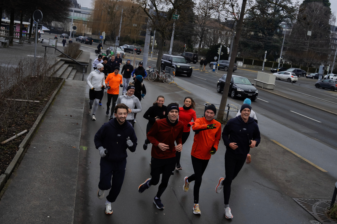 Athlix running group jogging along a wet city pavement in beanies and running jackets on a cold, grey day