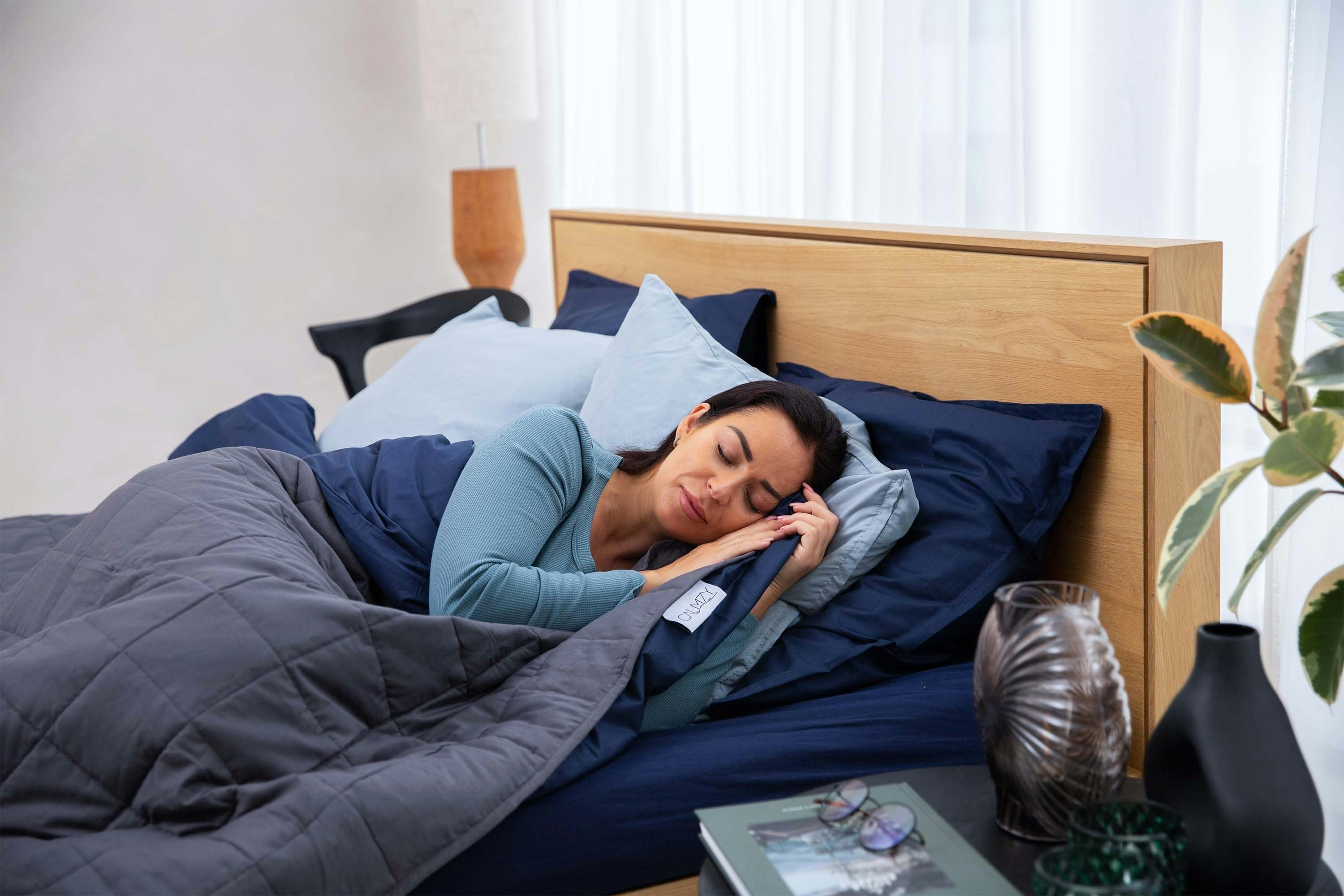 Frau schläft entspannt in einem modernen Bett mit dunkler Bettwäsche und hellen Kissen
