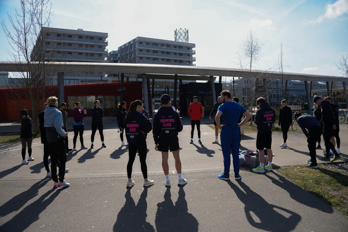 Laufgruppe in Running-Club-Hoodies steht im Kreis auf einem Platz und bespricht sich vor dem Training