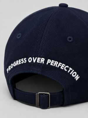 Nahaufnahme der Rückseite einer dunkelblauen Cap mit Schriftzug Progress over Perfection