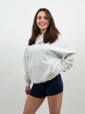 Frau im hellgrau melierten Hoodie mit blauem AP-Logo auf der Brust und dunkelblauen Shorts