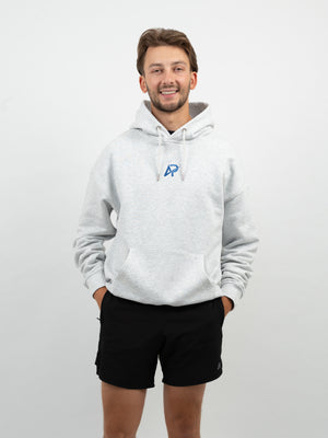 Mann im hellgrau melierten Hoodie mit blauem AP-Logo auf der Brust und schwarzen Shorts