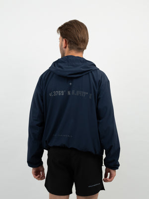 Mann von hinten im dunkelblauen Kapuzen-Windbreaker mit Koordinaten-Print auf dem Rücken