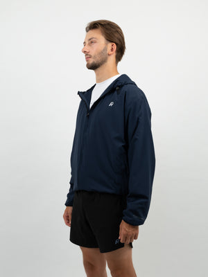 Mann im dunkelblauen Windbreaker mit weissem AP-Logo auf der Brust und schwarzen Shorts