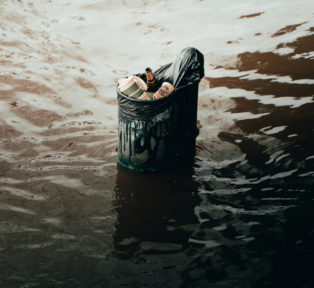 Überfüllter Mülleimer mit Plastikbechern und Glasflasche treibt im Wasser